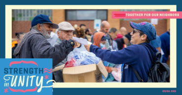 A woman hands a man a piece of paper at a charity event. The words "strength in unity" and "together for our neighbors" is shown. 